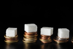 Sugar cubes stacked on piles of coins symbolizing the rising cost of sugar and taxation